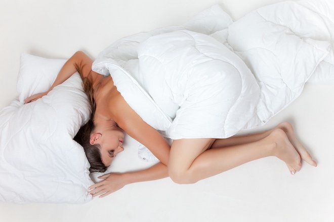 ベッドでシーツを被る女性