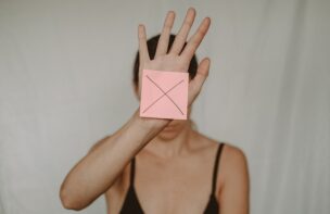 ×と書いたピンクの紙を手で顔が見えないように広げる女性