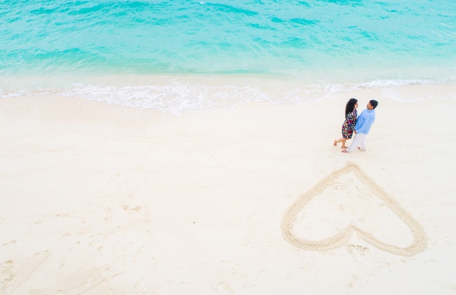 ビーチの砂場に描かれたハート側のカップル