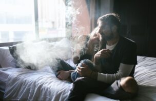 ベッドの上で寄り添いタバコをふかすカップル