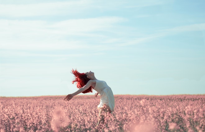 ピンクの草原に手を広げて空を仰ぐ女性