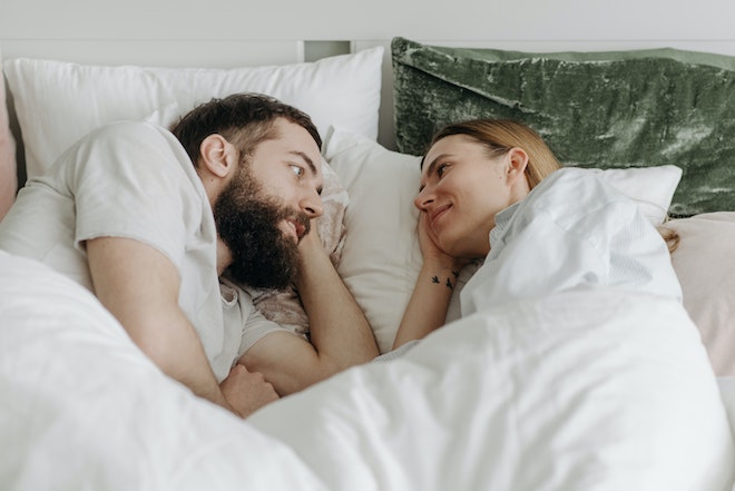 ベッドに横たわりながら、顔を見合わせるカップル